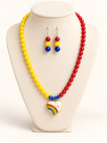 Yellow and red color-block beaded necklace with enamel rainbow heart pendant and matching red, yellow, and blue drop earrings on a cream bust