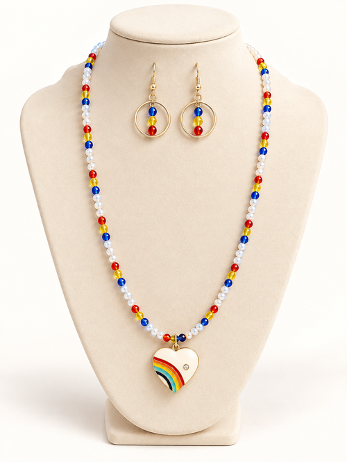 Pearl-look beaded necklace with red, yellow, and blue beads and an enamel rainbow heart pendant, with gold-tone hoop drop earrings on a cream bust