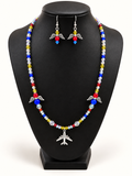 Iridescent beaded necklace with red, yellow, and blue accents, two angel-wing charms, and a silver-tone airplane pendant, with matching angel-wing earrings on a black bust