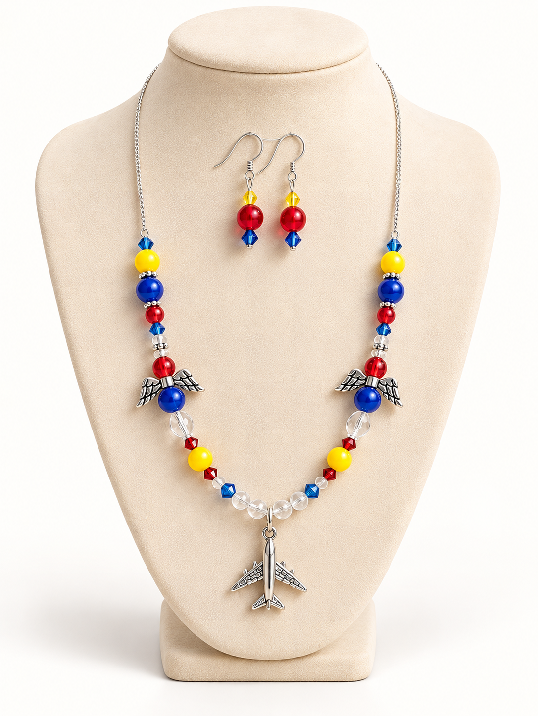 Silver-tone chain necklace with a beaded front section, two angel-wing charms, and an airplane pendant, with matching drop earrings on a cream bust